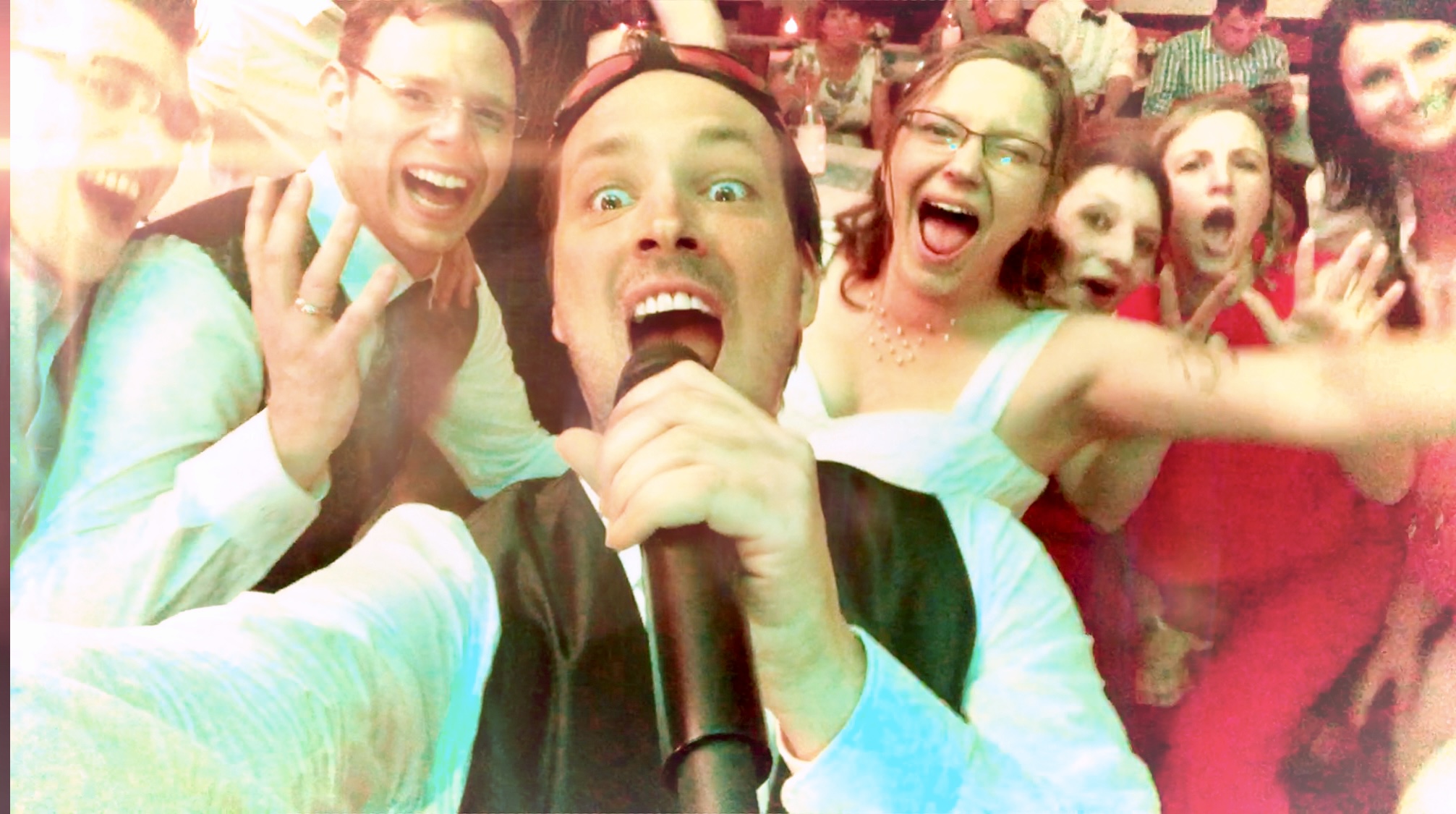 Mittendrin im Partygeschehen: Sing-DJ Rico Klemm schießt ein Selfie mit einer begeisterten Hochzeitsgesellschaft. Alle, inklusive der Braut, singen und jubeln voller Energie in die Kamera – ein Beweis für eine unvergessliche Feier.