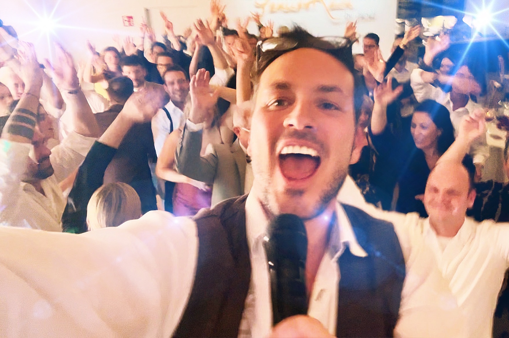 Pure Euphorie auf der Tanzfläche: Sing-DJ Rico Klemm fängt in einem energiegeladenen Selfie die jubelnde Partymenge mit erhobenen Händen ein.