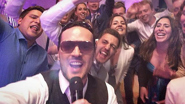 Vorschaubild zum Video: Sing-DJ Rico singt mit Mikrofon inmitten feiernder Gäste auf einer Hochzeitsparty.