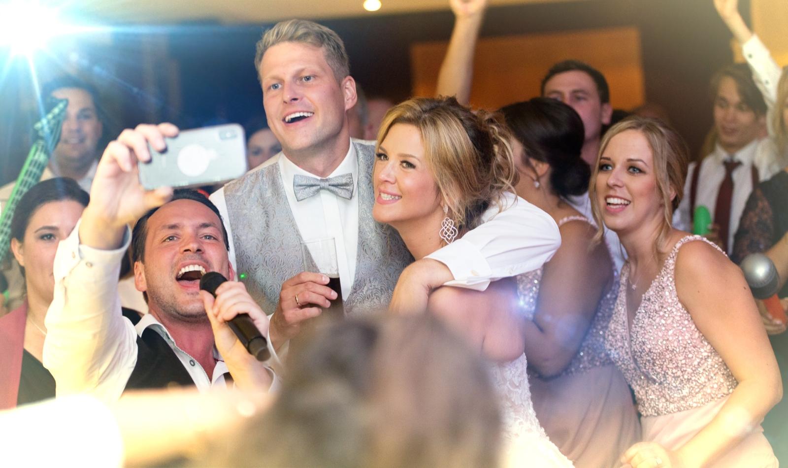 Sing-DJ Rico als Hochzeitssänger und DJ auf einer Feier, macht ein Selfie mit der tanzenden Menge.