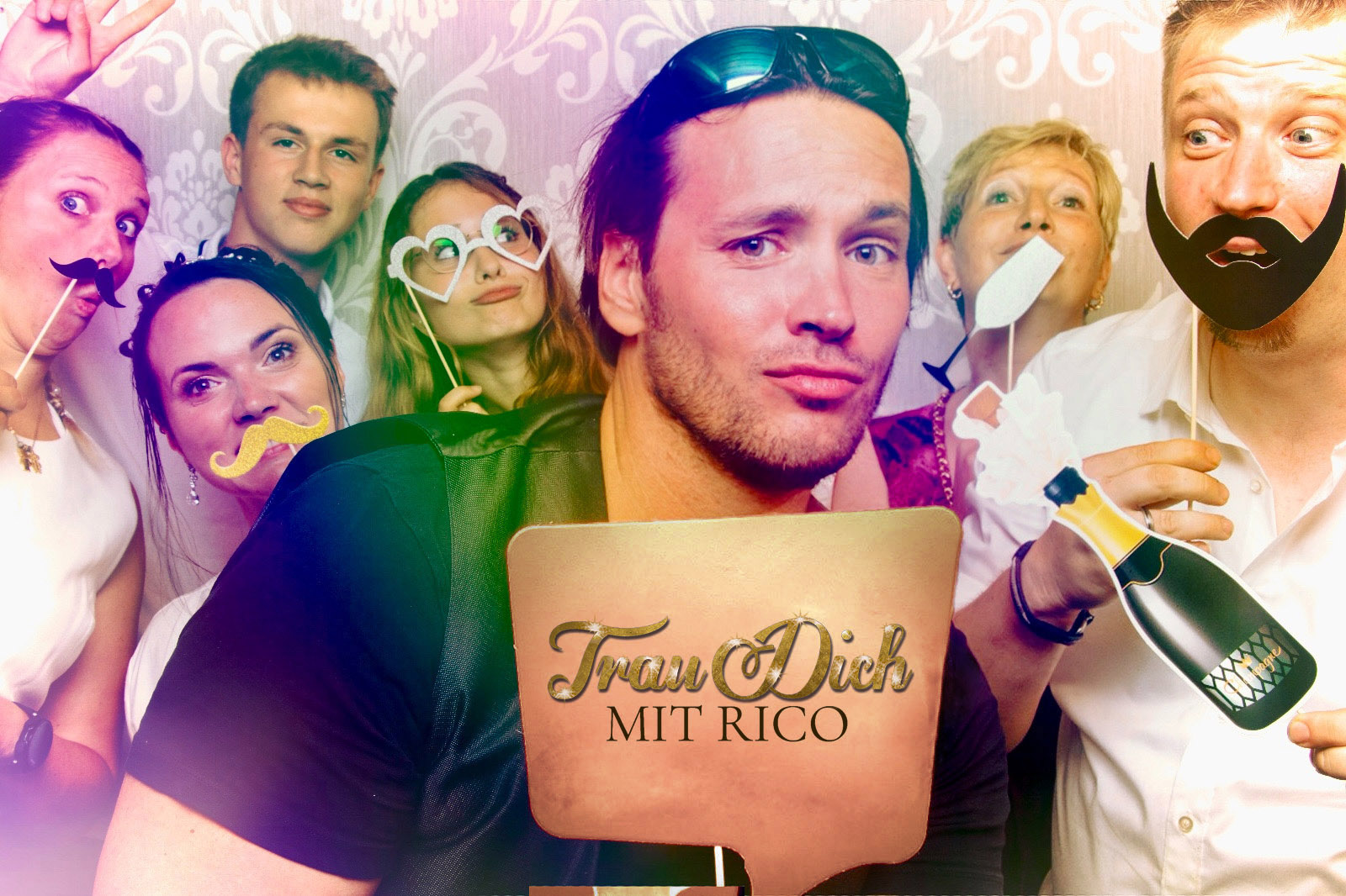 Sing-DJ Rico Klemm feiert mitten unter den Hochzeitsgästen und posiert für ein lustiges Foto in der Fotobox mit seinem 'TRAU DICH MIT RICO'-Schild.
